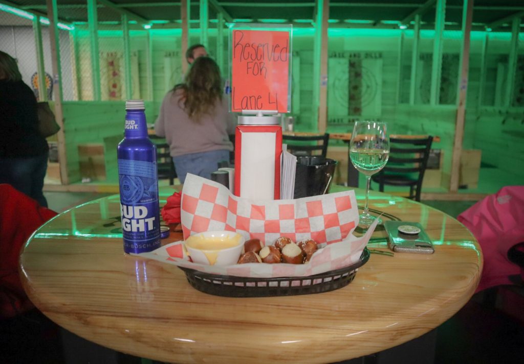 Socially distanced seating. A table in front of axe throwing lanes with pretzels, beer cheese, bud light, and wine.